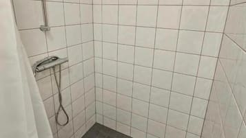 Ett litet, kaklat duschutrymme med ett avlopp, ett duschmunstycke och ett handhållet duschmunstycke.
