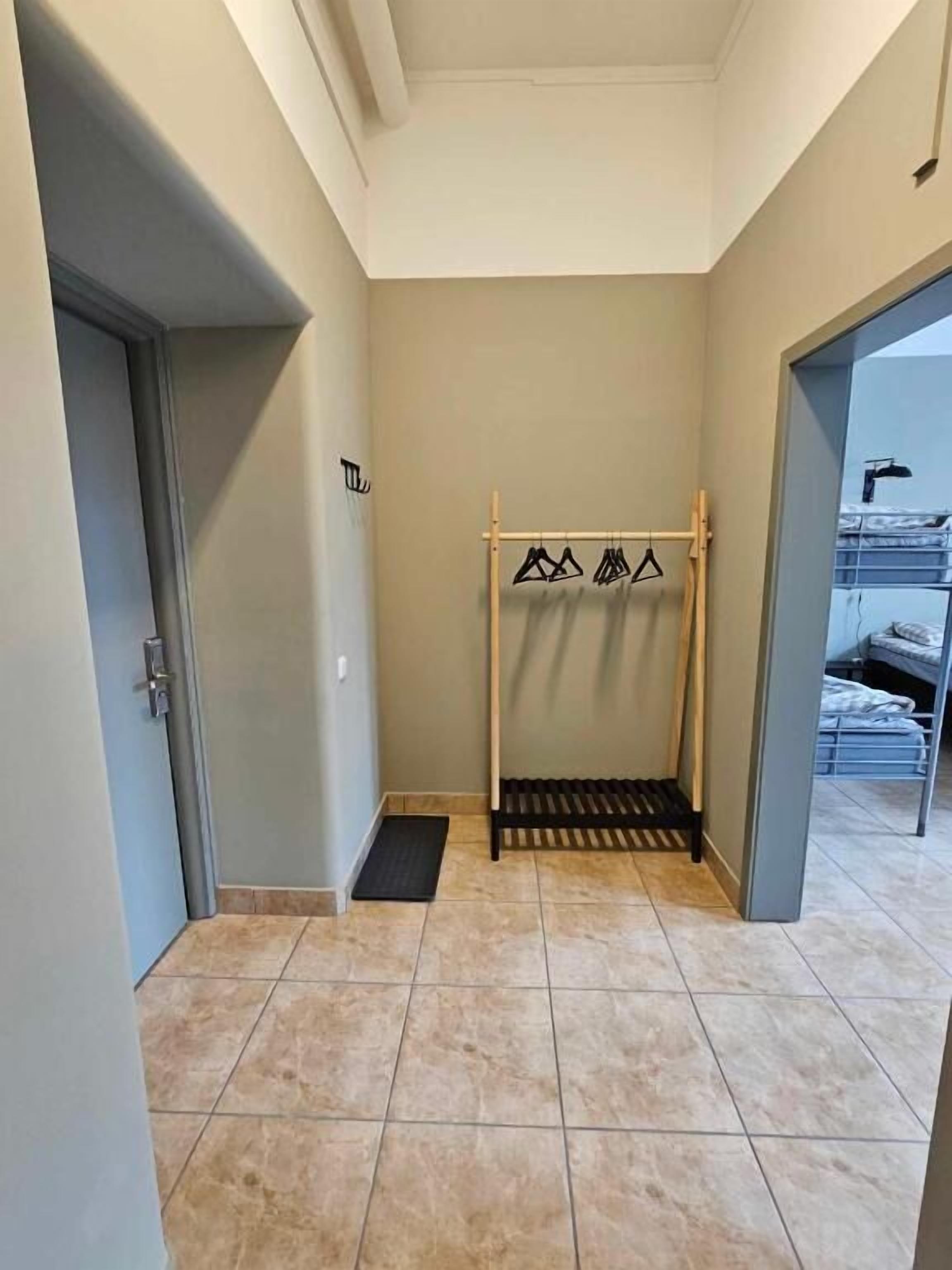 Corredor com um porta-toalhas de madeira, uma porta à esquerda e uma cama ao fundo.