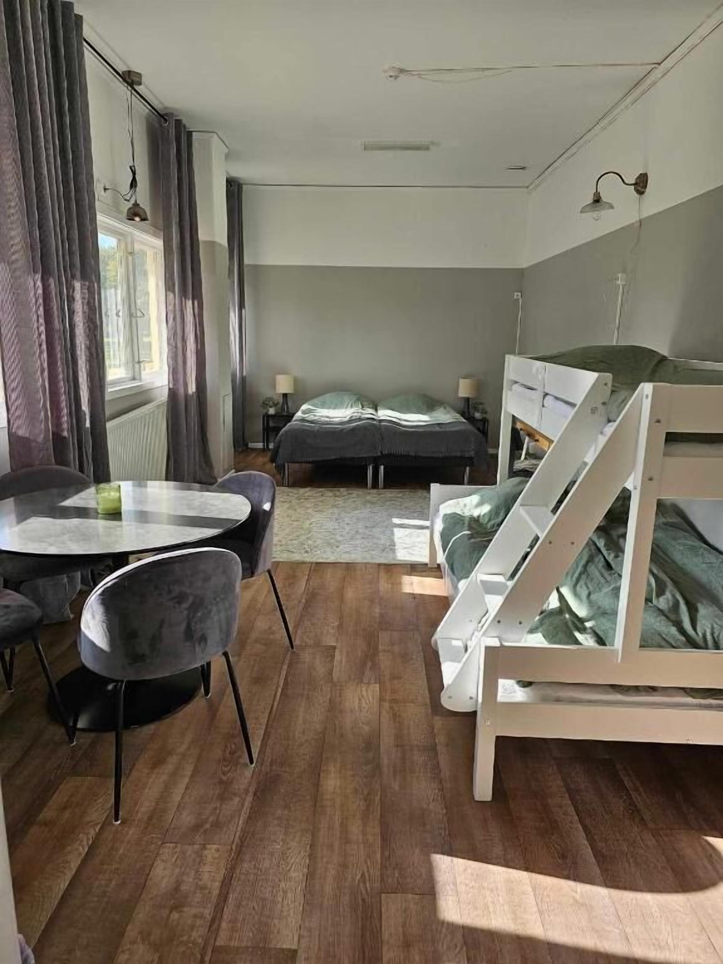 A bedroom with a bunk bed, a round dining table with chairs, and a window with curtains.