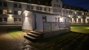 Un edificio con una pequeña estructura iluminada a su lado, un camino pavimentado y una zona ajardinada.