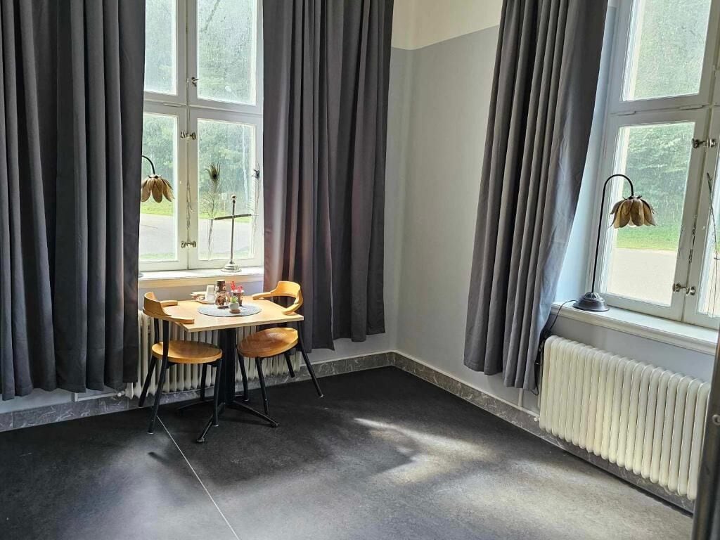 Um quarto com uma mesa, cadeiras, um radiador e uma janela com cortinas.