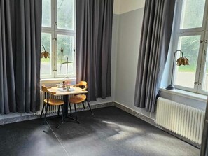 Una habitación con una mesa, sillas, un radiador y una ventana con cortinas.
