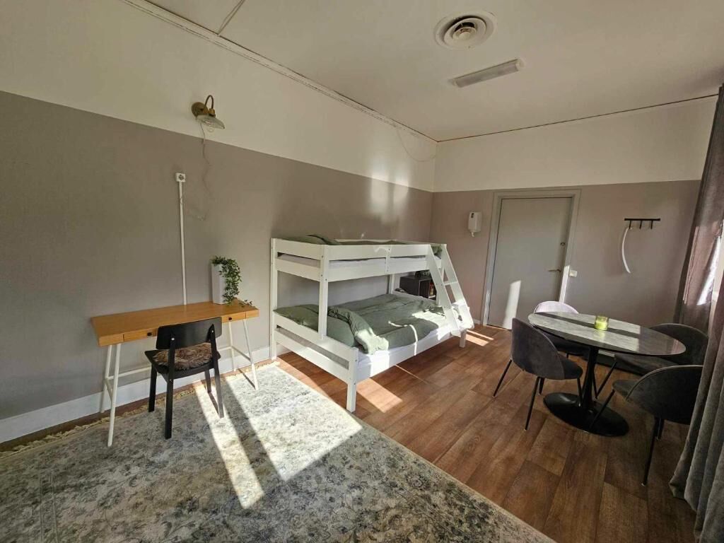 Et værelse med køjeseng, skrivebord, stol, spisebord med stole og en lille måtte.