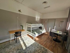 Una habitación con literas, un escritorio, una silla, una mesa de comedor con sillas y una pequeña alfombra.