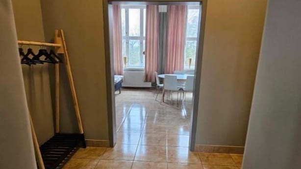 Un pasillo que conduce a una habitación con ventana, perchero y puerta.