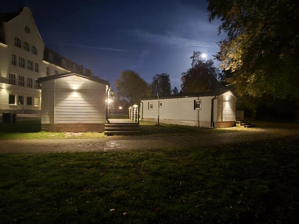 En byggnad med en överbyggd entré och trappsteg som leder upp till den, omgiven av gräs och träd.