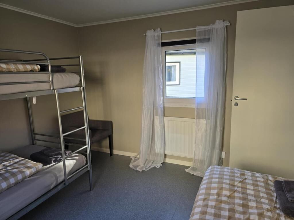 A room with bunk beds, a window with sheer curtains, and a door.