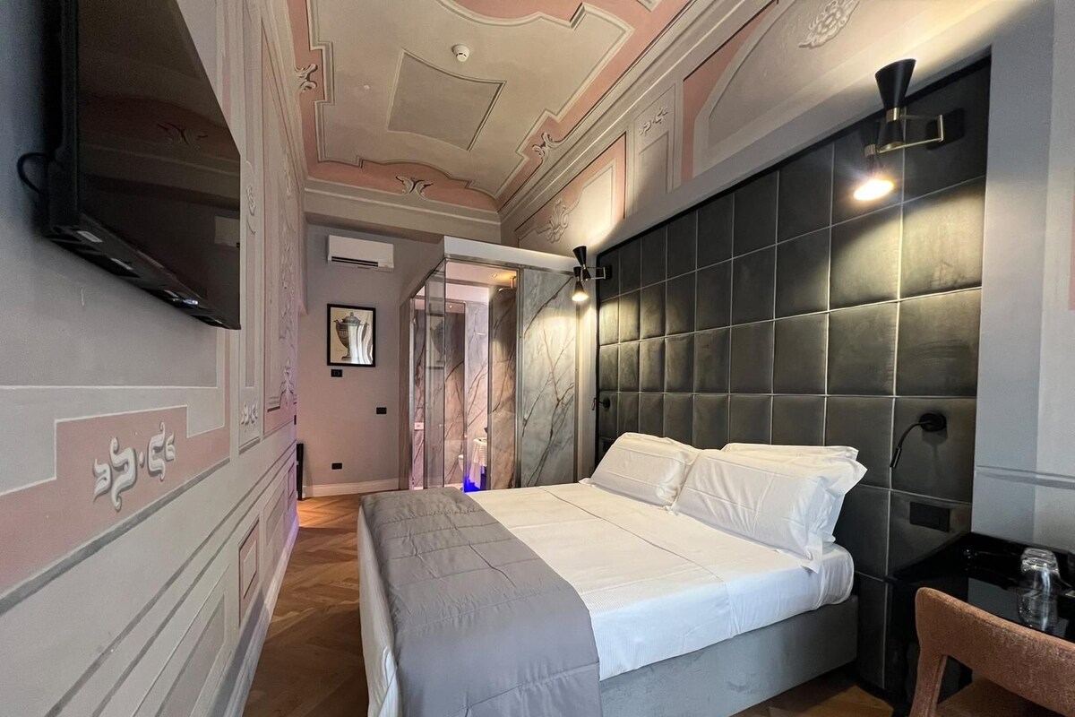 A bedroom with a bed, a TV, a bedside table, and a chair.