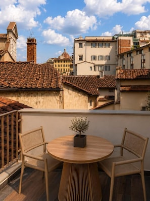 A terrace with a round wooden table and two wicker chairs, overlooking a cityscape with traditional buildings and a clear sky. - Vivaldi Boutique hotel (Florence)