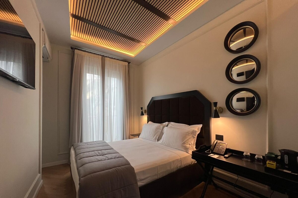 A hotel room with a bed, bedside table, lamp, and three wall-mounted mirrors.