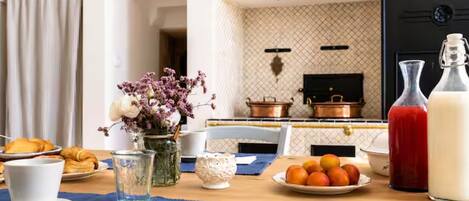 A breakfast setting with a table set for two, including croissants, a fruit plate, a glass of water, a vase with flowers, and a bottle of milk.