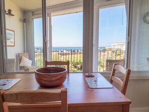 A dining area with a wooden table, chairs, a large wooden bowl, and a view of the beach through large windows. - 16 Old Shipyard Centre (Bridport)