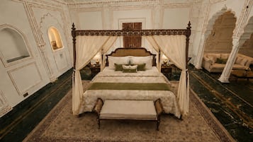A four-poster canopy bed with a green bedspread, a matching bench, and a large ornate rug.
