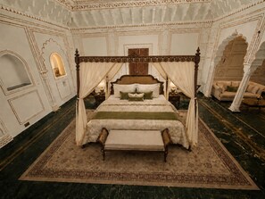 Una cama con dosel y cuatro columnas, con un edredón verde, un banco a juego y una alfombra grande y decorativa.