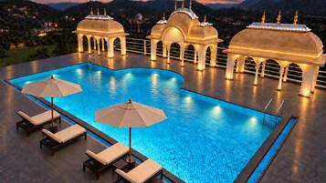 A swimming pool with lounge chairs and umbrellas, surrounded by ornate structures with domes and spires.