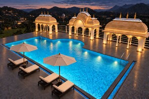 Una piscina con sillas de descanso y sombrillas, rodeada de estructuras ornamentales con cúpulas y agujas.