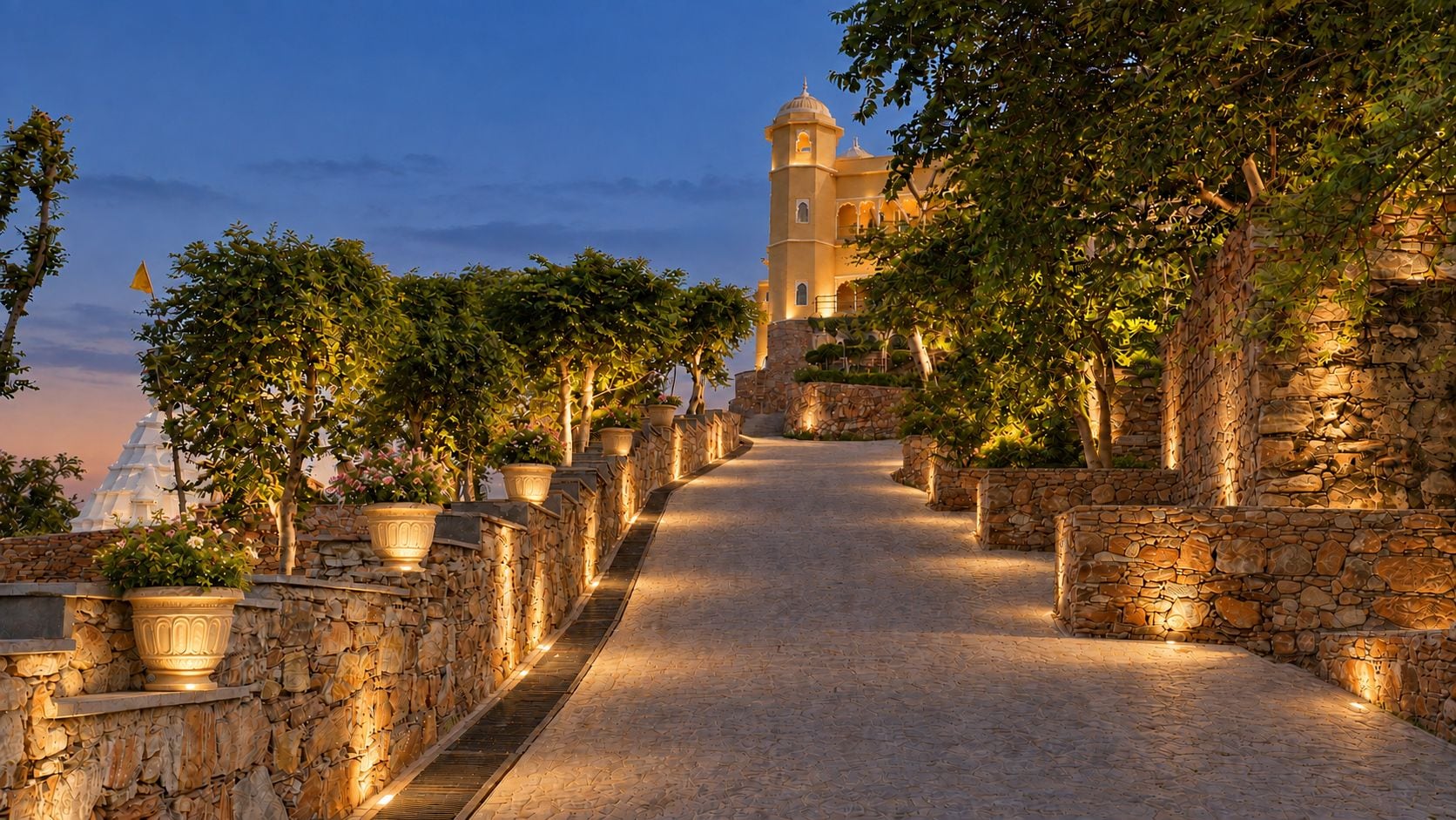 A pathway leading to a building with a tower, flanked by stone walls and potted plants.