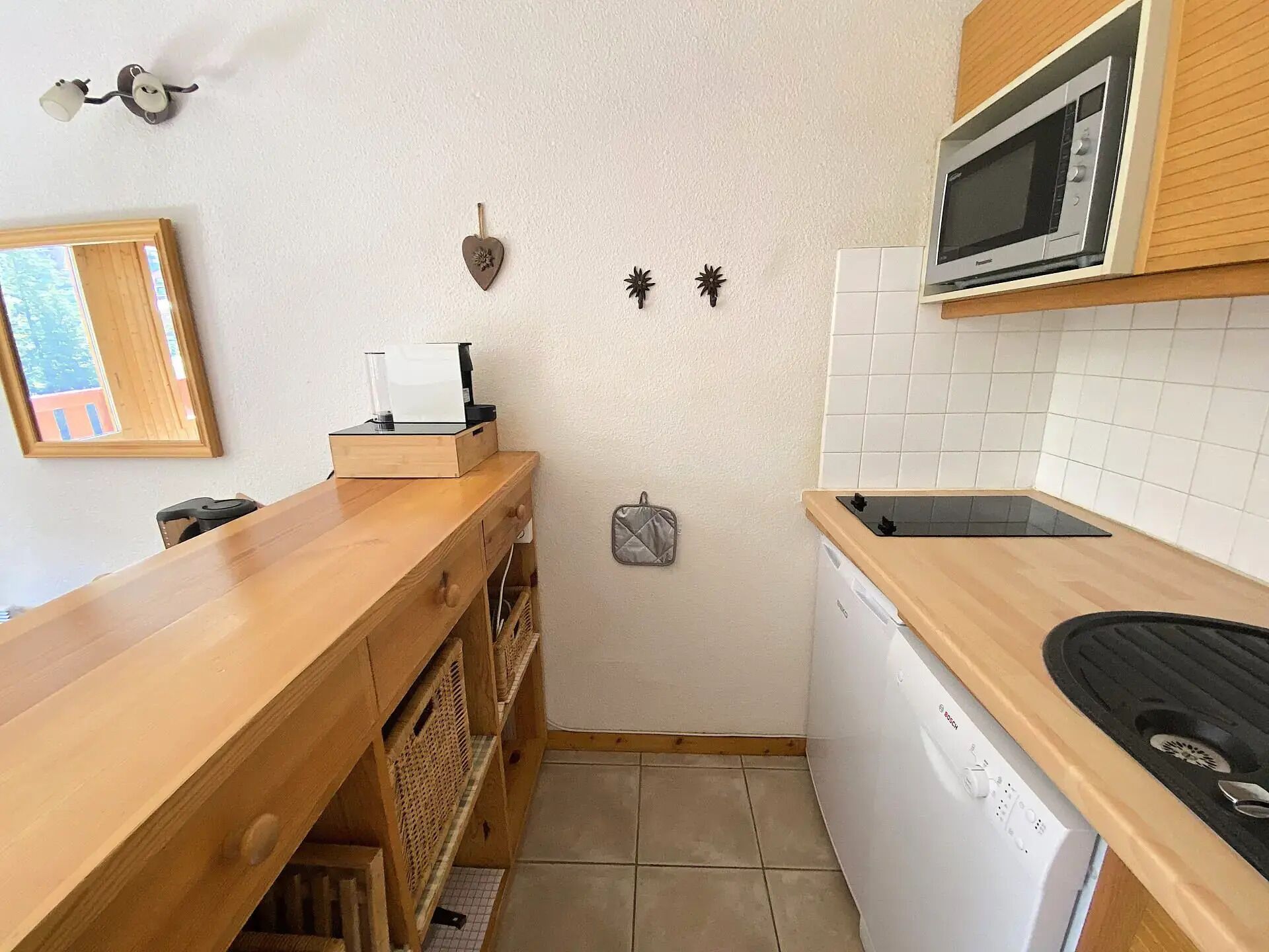 Een kleine keuken met een magnetron, vaatwasser en een houten aanrecht.