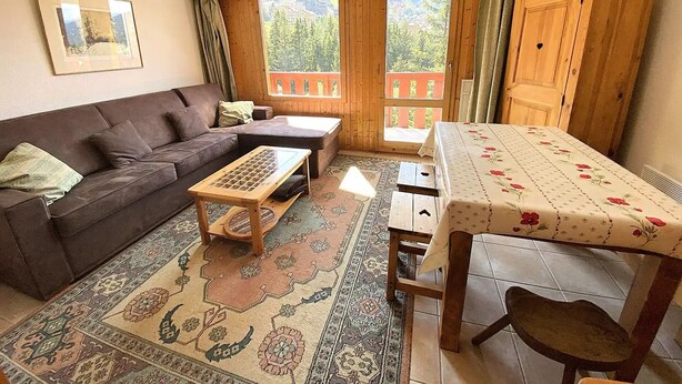 A cozy living room with a sofa, a coffee table, a dining table, and a view of a balcony. - Studio for 4 people at the entrance to Méribel Mottaret (LES ALLUES)