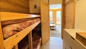 A room with a bunk bed, a wooden door leading to an outdoor area, and a kitchenette. - Studio for 4 people at the entrance to Méribel Mottaret (LES ALLUES)