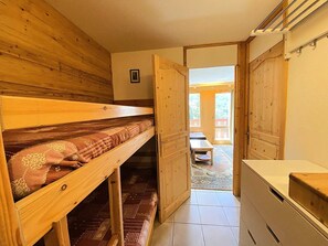 Ein Zimmer mit Etagenbett, einer Holztür zu einem Außenbereich und einer Küchenzeile.