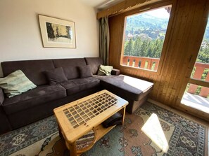 Ein gemütliches Wohnzimmer mit einem dunkelbraunen Sofa, einem Holztisch und einem großen Fenster mit Blick auf ein bewaldetes Gebiet.