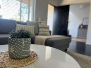 A modern living room with a round white coffee table, a decorative plant in a textured pot, and a sofa with cushions. - Relax, Gather& Explore | 5 Bedroom Highlands Home (Moss Vale)