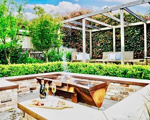 An outdoor barbecue area with a grill, a table with a bottle and glass, and a wooden bench. - Relax, Gather& Explore | 5 Bedroom Highlands Home (Moss Vale)