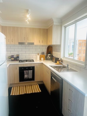 A modern kitchen with wooden cabinets, a built-in dishwasher, and a window providing a view of the outside. - Relax, Gather& Explore | 5 Bedroom Highlands Home (Moss Vale)