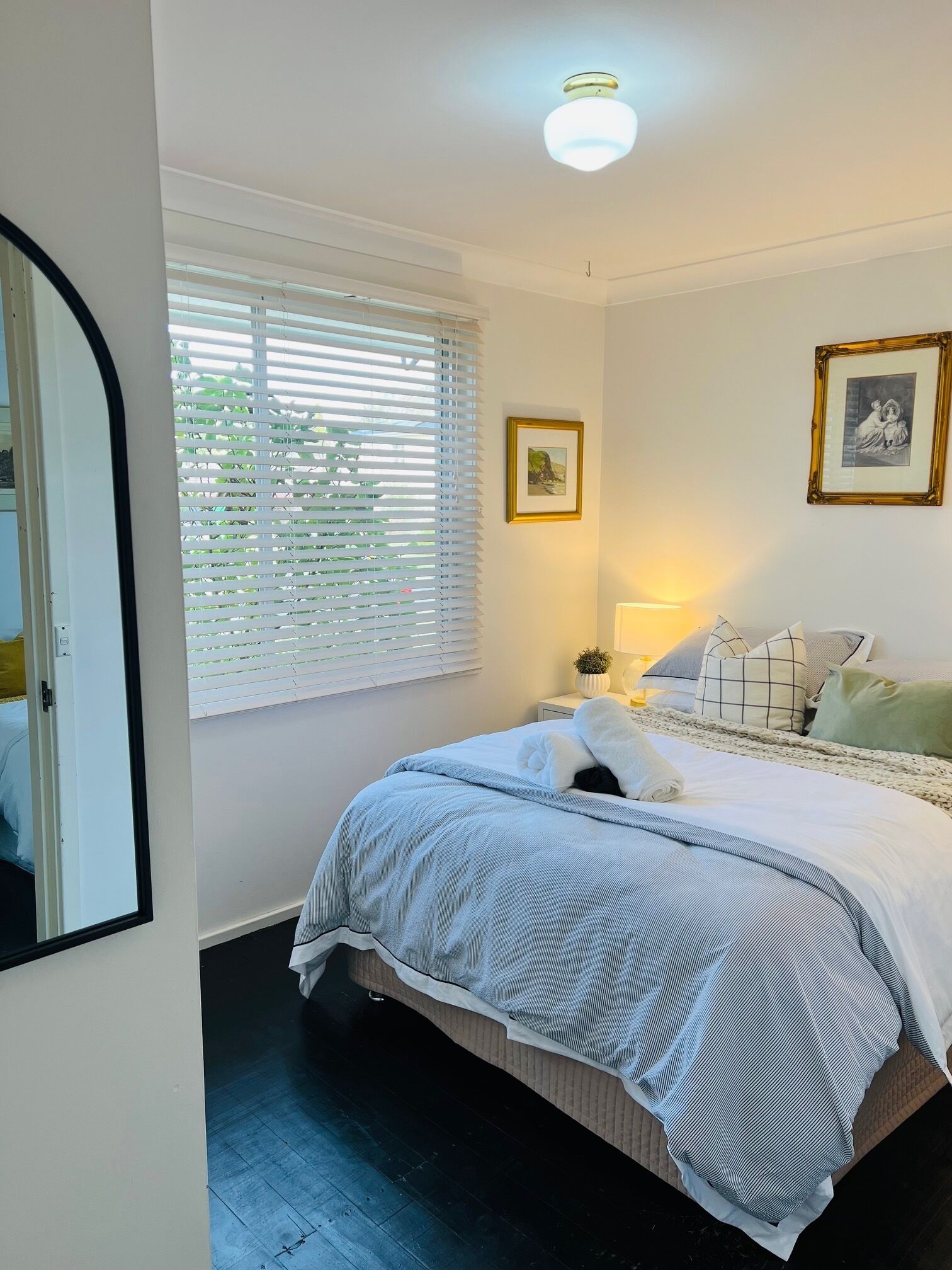 Une chambre à coucher avec un lit, une table de chevet, une lampe et deux tableaux encadrés accrochés au mur.