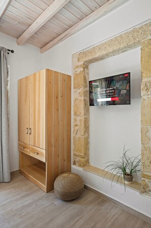 A room with a wooden wardrobe, a mounted television displaying a streaming service, and a stone wall. - Villa Papadia with Private Pool – Pitsidia, South Crete (Iraklio)