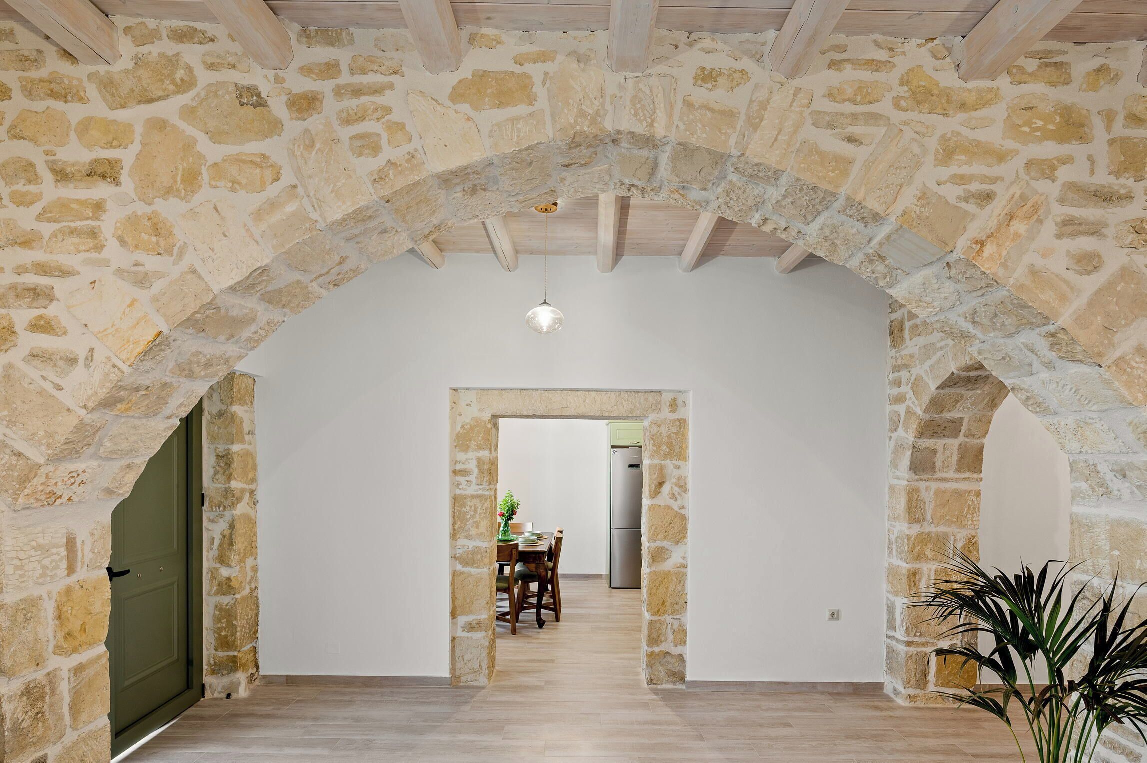 Un arco de piedra que conduce a un comedor con una mesa y sillas, una lámpara colgante y una planta en maceta.