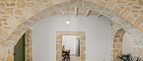 Un arco de piedra que conduce a un comedor con una mesa y sillas, una lámpara colgante y una planta en maceta.
