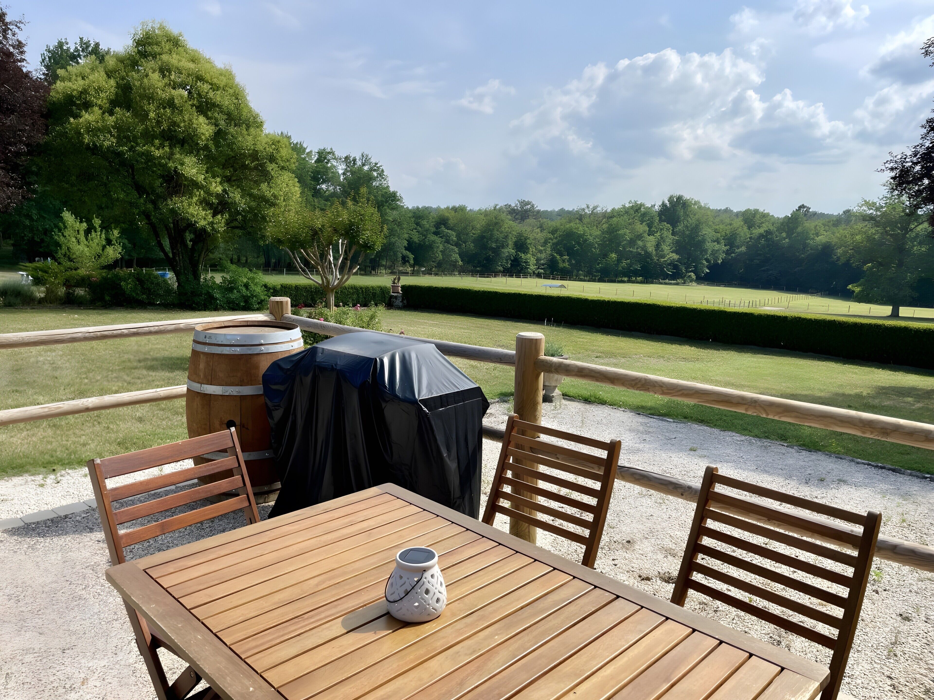 An outdoor seating area with a table and chairs, a covered grill, and a view of a green landscape.