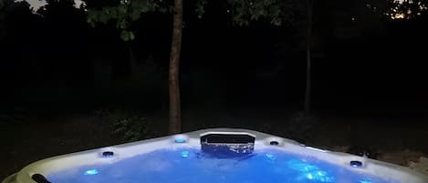 A hot tub with a blue light feature, surrounded by trees.