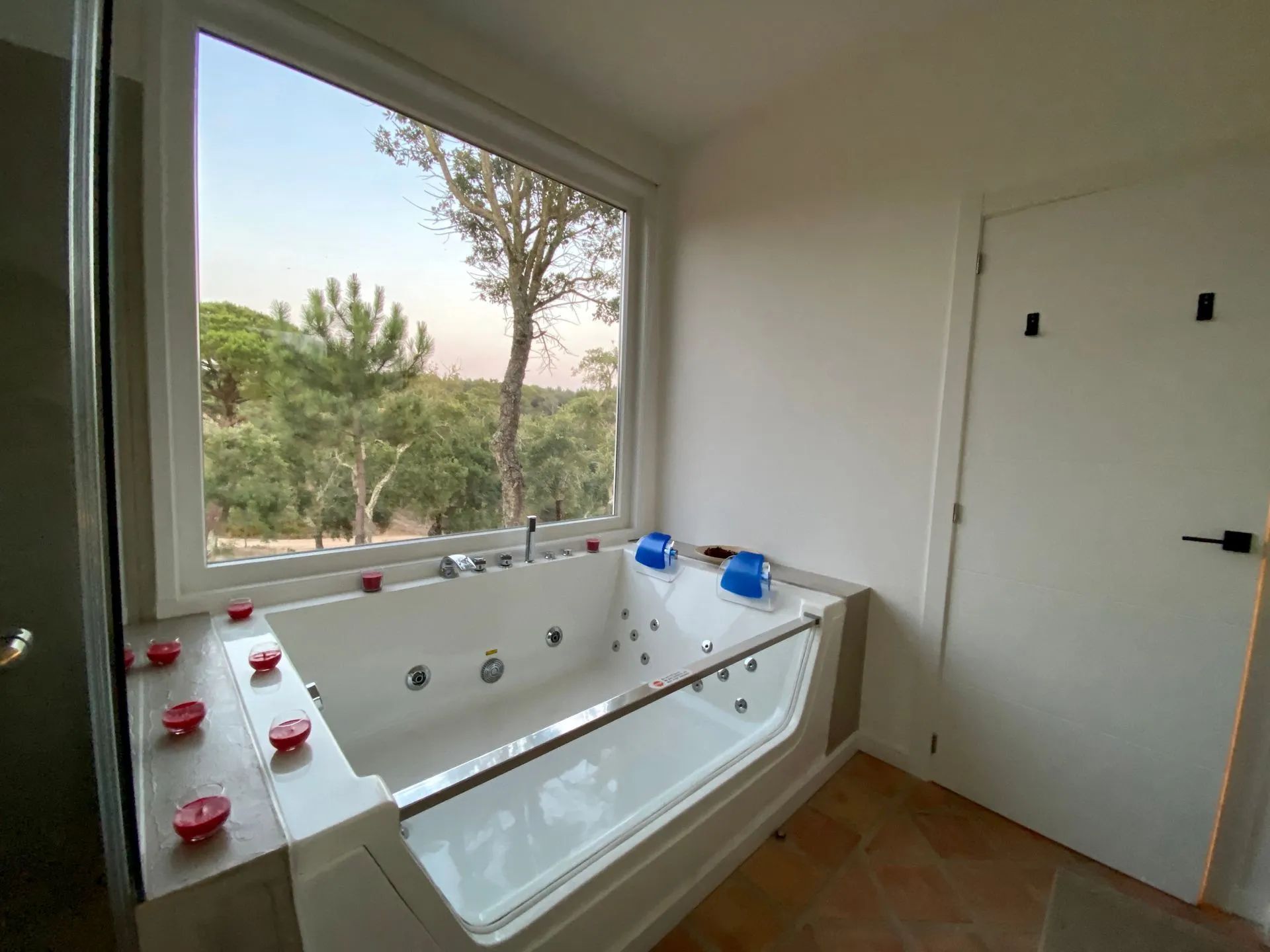 Um banheiro moderno com uma banheira grande, uma janela com vista para árvores e uma porta.