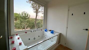 Um banheiro moderno com uma banheira grande, uma janela com vista para árvores e uma porta.
