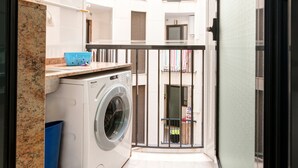 A laundry area with a washing machine, a blue laundry basket, and a small table with a towel rack. - Apartment 'Beach' with Sea View, Wi-Fi and Air Conditioning (Alboraya)