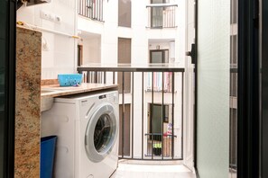A laundry area with a washing machine, a blue laundry basket, and a small table with a towel rack. - Apartment 'Beach' with Sea View, Wi-Fi and Air Conditioning (Alboraya)