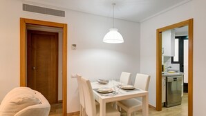 A dining area with a table set for four, white chairs, a white pendant light, and a wooden door. - Apartment 'Beach' with Sea View, Wi-Fi and Air Conditioning (Alboraya)