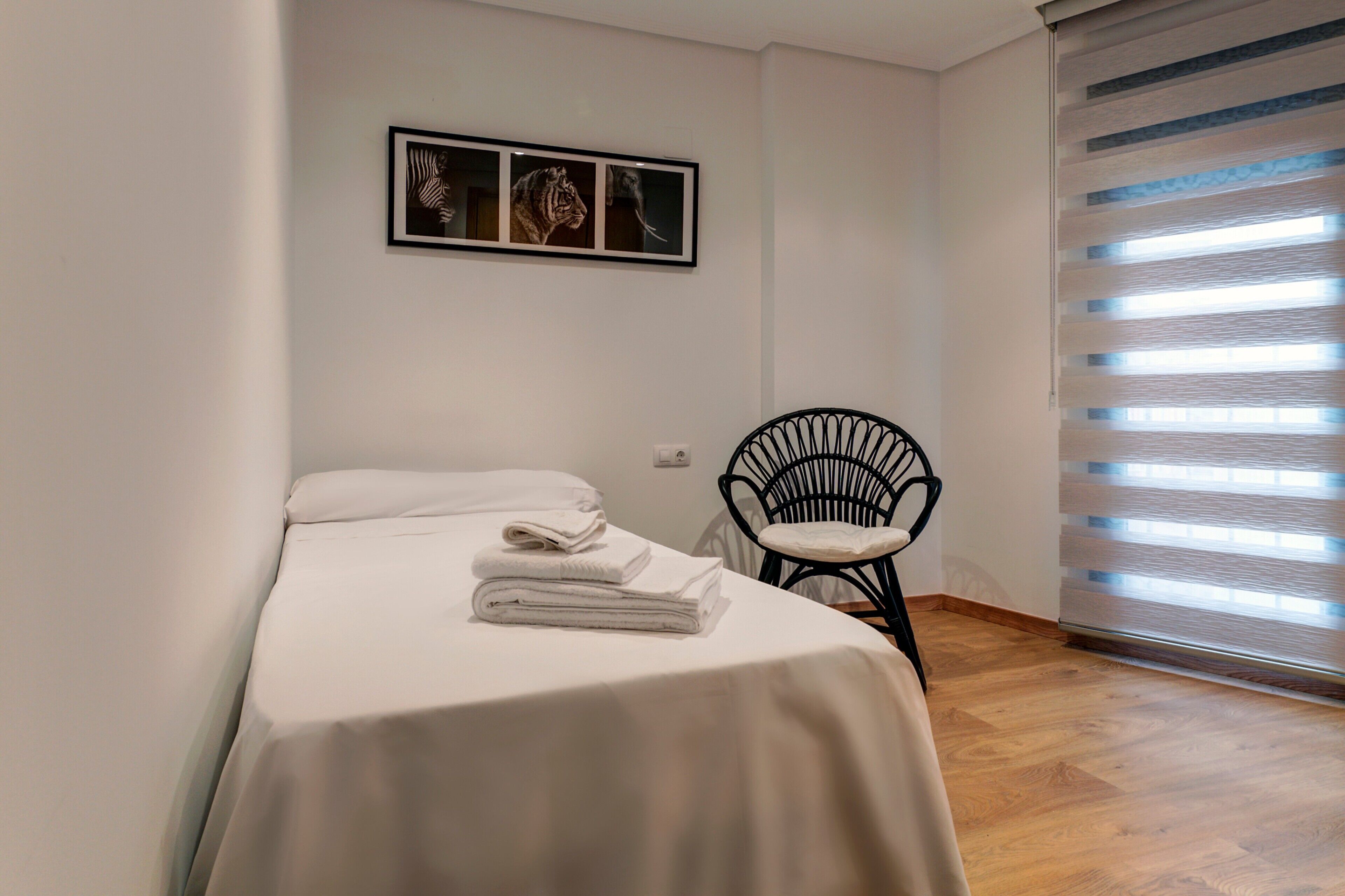 A bedroom with a bed, a chair, and a window with blinds.