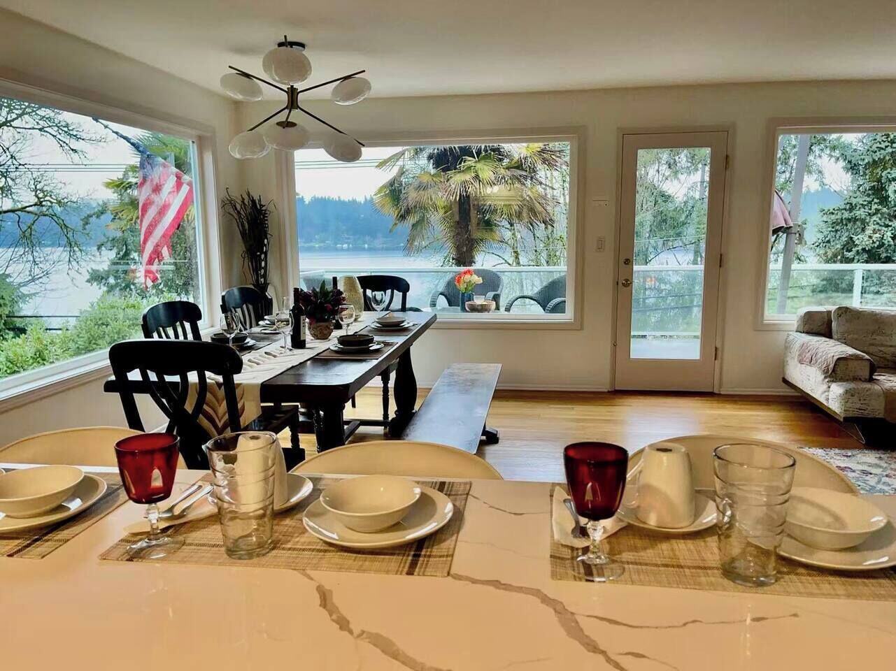 A dining area with a table set for four, a bench, and a view of the outdoors through large windows.