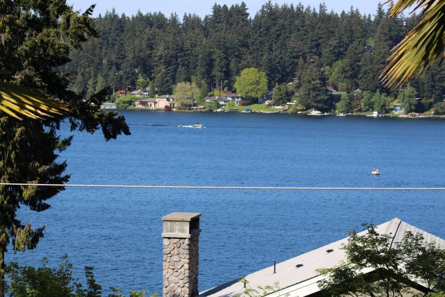 Un lago con un puente colgante, casas al fondo y una chimenea de piedra en primer plano.