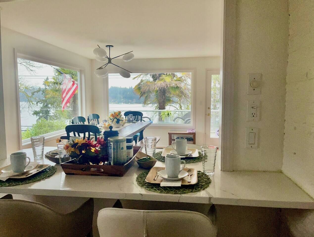 A dining area with a table set for four, a ceiling fan, and a view of the outdoors through large windows.