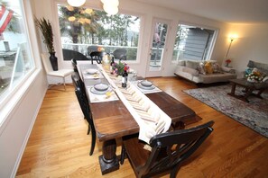 A dining area with a wooden table set for four, surrounded by chairs, with a view of the outdoors through large windows. - Luxury 180 degree Lake View N Mercer Island Home 1 (Mercer Island)