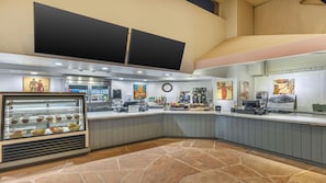 Un mostrador de panadería con una vitrina de productos horneados, una máquina de café y un reloj en la pared.
