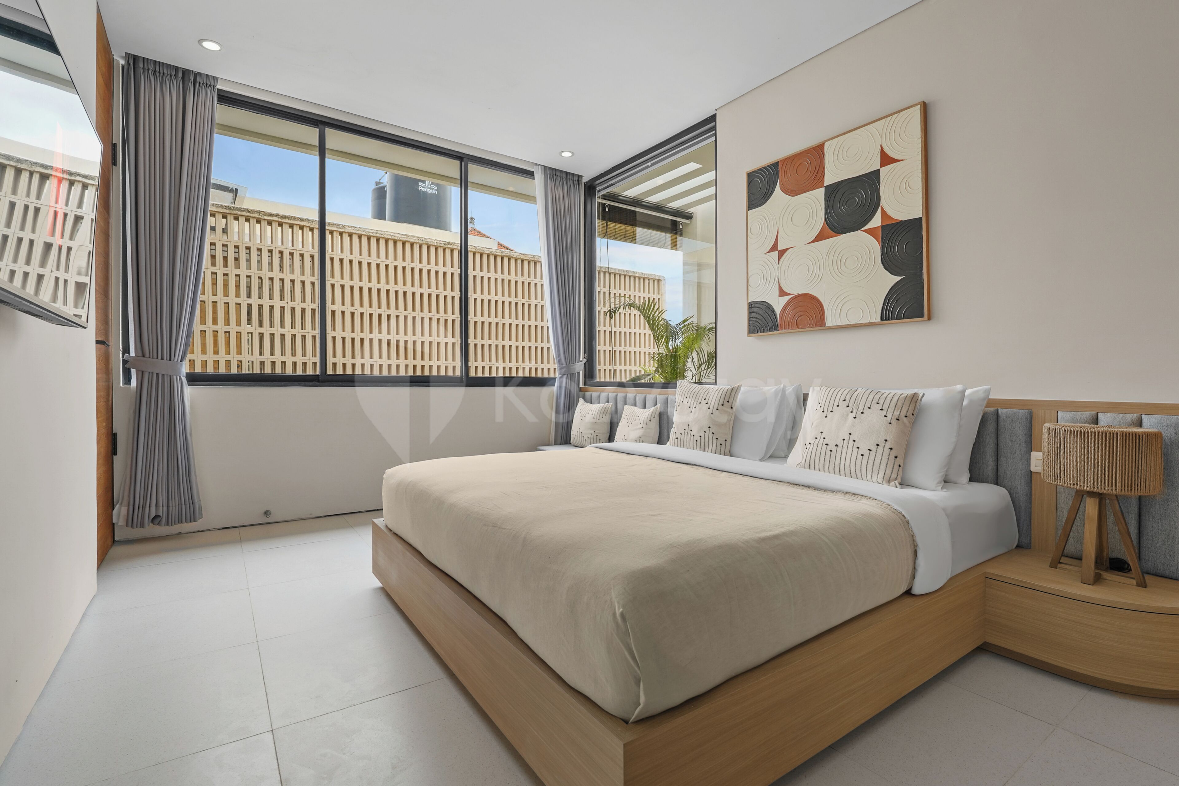 A modern bedroom with a large bed, a view of buildings through the window, and a piece of abstract art on the wall.