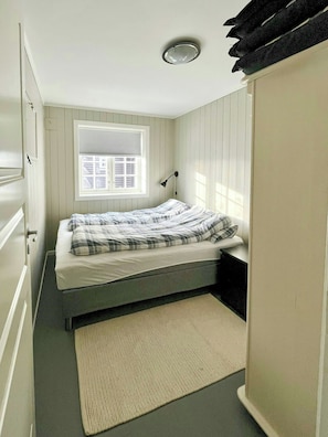 Ein Schlafzimmer mit Bett, Fenster mit Jalousien, Nachttischlampe und Tür.