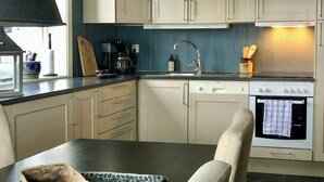 A kitchen with white cabinets, a stove, a sink, and a dining area with a table and chairs. - Ski-in/ski-out flat in Gaustablikk (Rjukan)