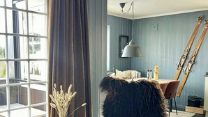 A room with a large window, a chair with a fur throw, a small table with a vase, and a dining area with a table and chairs. - Ski-in/ski-out flat in Gaustablikk (Rjukan)